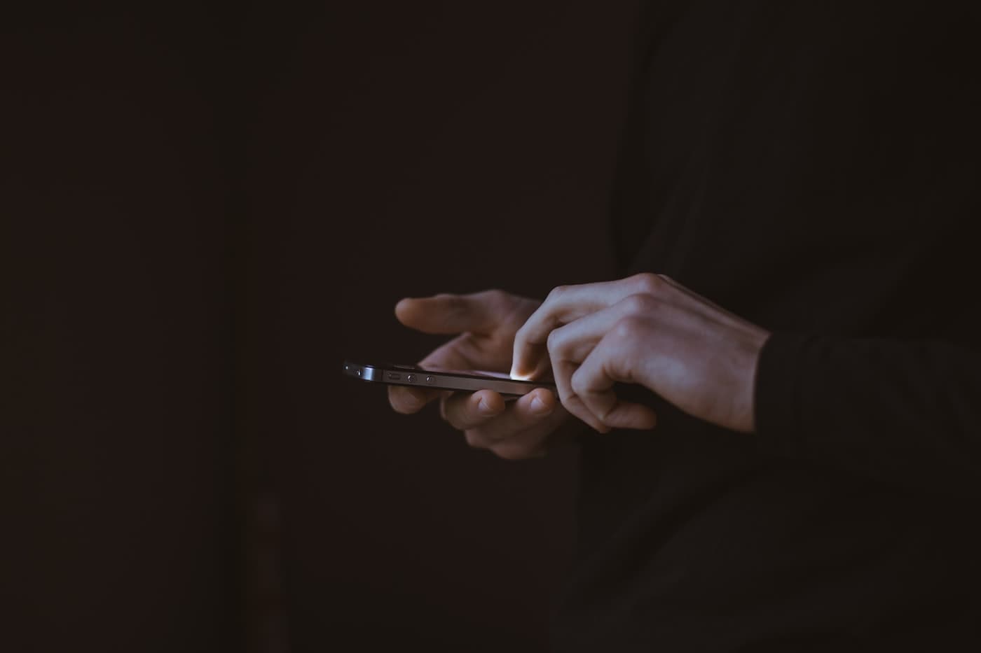 A pair of hands using a phone in near darkness, the screen the only light source.
